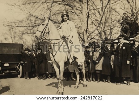 Inez Milholland, wearing white robes and a crown riding a white horse as the \'Herald\' in the Women\'s Suffrage parade of March 3, 1913, the day prior to Woodrow Wilson\'s inauguration.