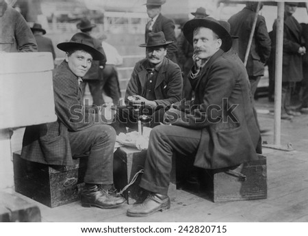 Three cheerful men (probably Germans), share a meal and a bottle on the immigrant ship the PRESIDENT GRANT of the Hamburg American Line at the end of its voyage in New York Harbor. Ca. 1910.