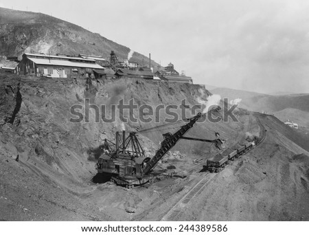Open pit United Verde Mine on mountain side in Jerome, Arizona. Photo shows a crane strip mining raw copper ore and depositing it into open railroad cars. Ca. 1915.