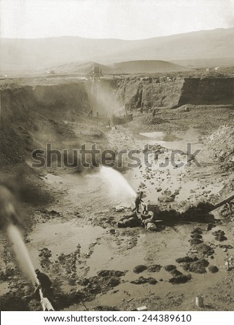 Alaskan hydraulic gold mining used jets of water to erode rock material or move sediment. The resulting water-sediment was then directed through sluice boxes to remove the gold.Ca. 1900-1923.