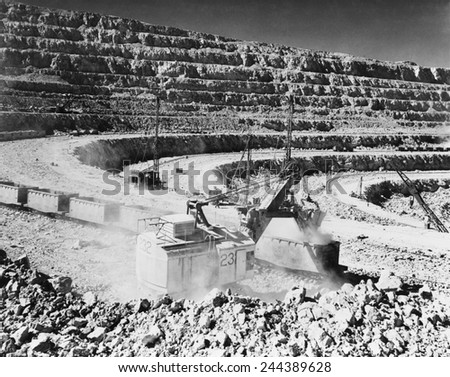 Open pit copper mine at Chuquicamata, Chile. Photo shows a crane steam shovel strip mining raw copper ore and depositing it into open railroad cars. Ca. 1945.
