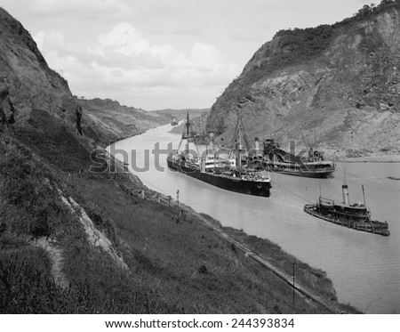 Boats move through Panama Canal at the Culebra Cut (Gaillard Cut), which crosses the continental divide. At center right is a suction dredge to maintain canal depth. Ca. 1910-14.