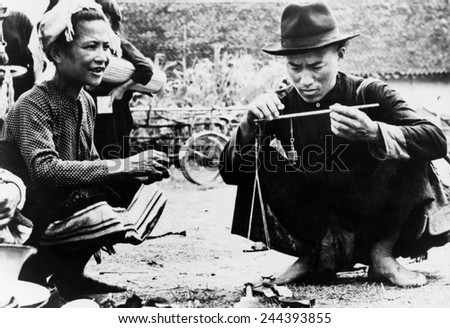 Drug seller openly weighing opium for a customer in an outdoor market in Laos. 1954.