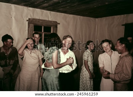Square dance in rural home in McIntosh County Oklahoma. They dance in a simple interior with butcher paper covered walls. Ca. 1938-39.