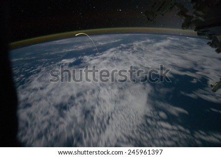 Space shuttle Atlantis re-entry flight path resembles a bean sprout against clouds and city lights. Photograph by the Expedition 28 crew in the International Space Station. May 23, 2011.