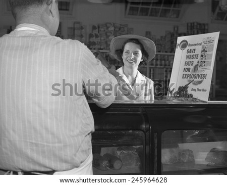 Women at grocery store meat counter. A sign on a grocery store counter reads ' Housewives-Save Waste Fats for Explosives-Bring Them Here'.