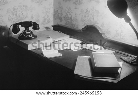 A US government clerk\'s home office desk with books, telephone and directory, and a desk lamp. Washington, D.C. 1939.
