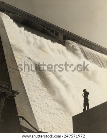 A workman inspecting the Grand Coulee Dam from the partially-complete wall near the east powerhouse, July 20, 1942.