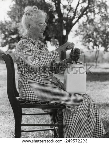 Elderly farm woman using a small glass butter churn. Oklahoma, July 1935.