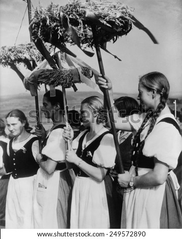German women wearing traditional folk costumes during the 1935 Erntedankfest. \'Peasant women\' hold beribboned wreaths with during the Nazi celebration.