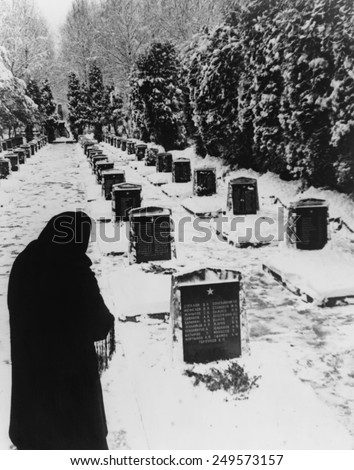 Russian woman in a snow-covered military cemetery. WW2 Soviet tombstones are inscribed with several names. Unknown location. 1945 photo by Yevgeny Khaldei.