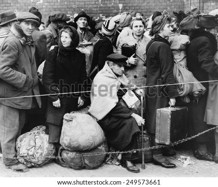 German displaced persons wait in Berlin\'s Anhalter Station in 1945. Refugees are carrying their few belongings, as the stand behind a rope and double strand of barbed wire.