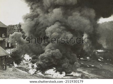 Smoke rises from a rubber factory destroyed by the retreating British forces in Malaya. Bales of rubber and machinery were destroyed to prevent their use by Japanese. Ca. Dec. 1941-Jan. 1942.