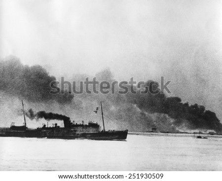 Ship leaving Dunkirk carrying defeated British and French soldiers to England. In the background the French port of Dunkirk burns under the German advance. World War 2. May 26-June 4, 1940.