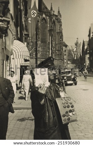 German street vendor sells Nazi political buttons on the street. Ca. 1930.