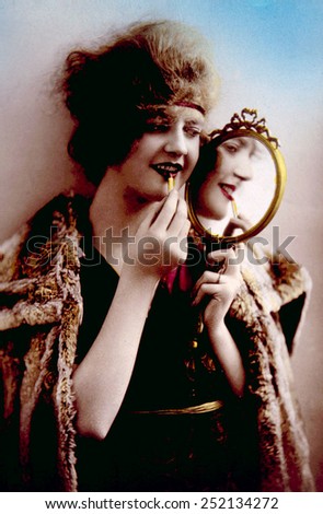 Women holding mirror while applying lipstick, circa. 1900.