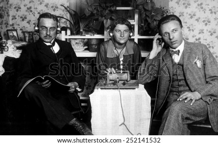 Three people listening to an early radio, c. 1925