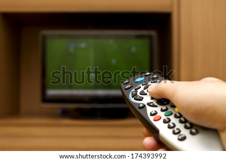 Hand holding TV remote control with a television football.