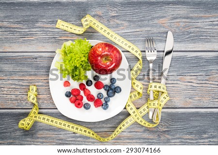 Fitness salad and measuring tape on rustic wooden table.