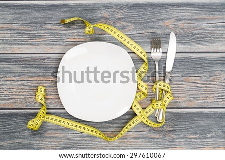 Empty plate with measure tape, knife and fork. Diet food on wooden table background.