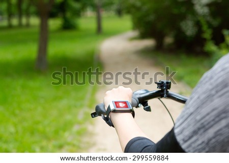 Woman riding a bike with a smartwatch heart rate monitor. Smart watch concept.