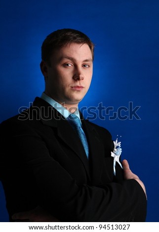 Portrait of young attractive dark-haired man wearing shirt and black jacket against blue background.