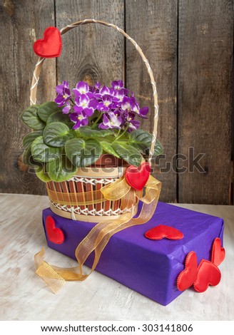 The basket of flowers violets and gift with hearts and gold ribbon