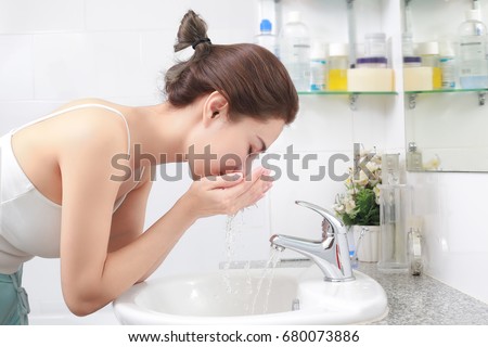 Woman washing her face with water above bathroom sink.