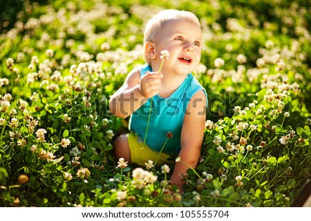 Little boy sitting in the grass picking clover with a cute expression on his face