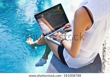 Woman working on her laptop computer sitting at poolside