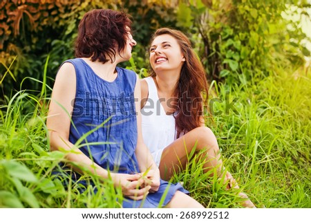 mother with grown up daughter sitting on a grass and affectionately talking