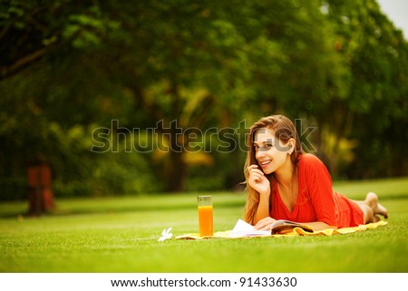Young woman on the grass with book and orange juice