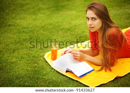 Young woman on the grass with book and orange juice