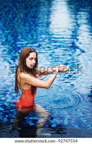 Young beautiful woman in water pool in luxury hotel in Bali, Indonesia holding water in her hands