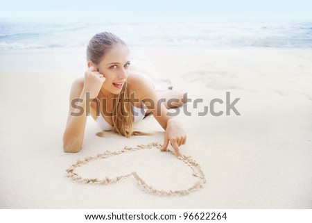 Love concept: young beautiful woman on the beach making heart on the sand