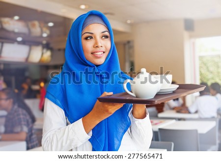 asian muslim waitress holding a tray with tea. Woman wearing hijab working in cafe