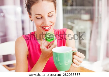 woman looking at macaroon she\'s going to eat. Lovely color combination of pink and green