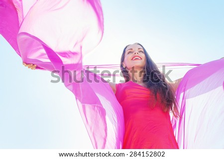 happy woman holding bright violet textile over blue sky