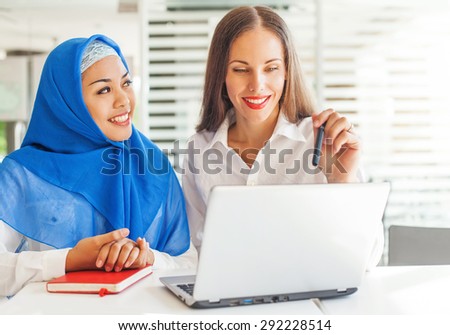 European woman and asian muslim woman working together on same project