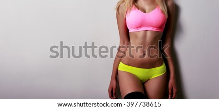 Beautiful sporty female body in pink and green bikini isolated on gray background