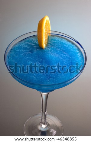 Frozen Blue Hawaiian mixed drink with orange slice garnish on grey background with reflection