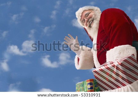 Santa Claus with bag of presents waves against a background of Cumulus clouds in an azure blue sky