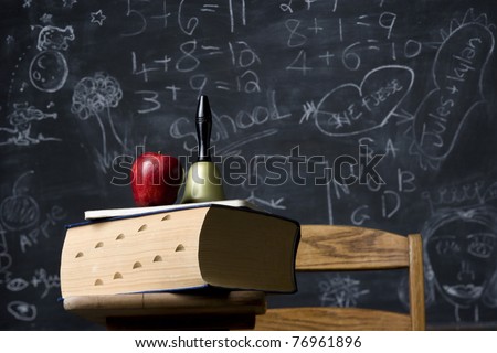 A classic still life of an antique school desk with huge dictionary and school bell against a blackboard. Horizontal shot.