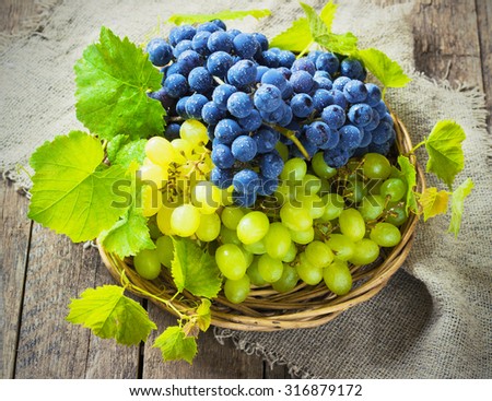 blue and green grapes in a basket on a wooden background toning