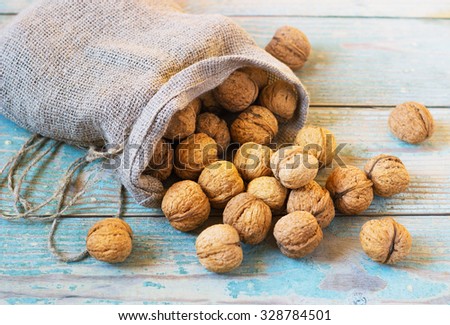 Pile of walnuts in shellin a bag on a wooden background . Linen sack with walnuts in the background.