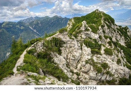 Narrow hiking trail leading along a stony mountain spine to the peak