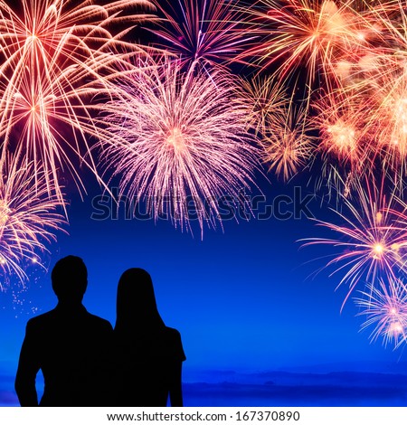 Spectacular fireworks display on deep blue sky with silhouettes of a young couple watching it