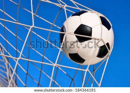 Football or soccer goal, with a neutral design ball flying into the net and blue sky in the background