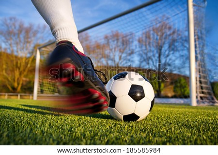 Football or soccer shot with a neutral design ball being kicked, with motion blur on the foot and natural background