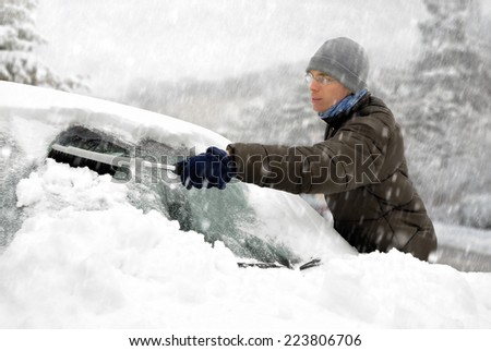 Young man brushing the snow off his car on a cold winter day in snowfall